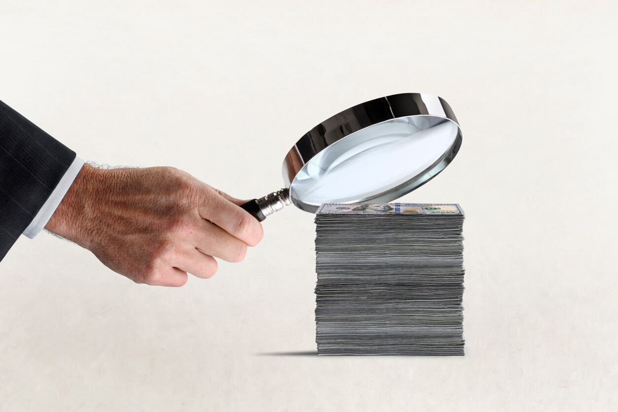 stack of cash under magnifying glass