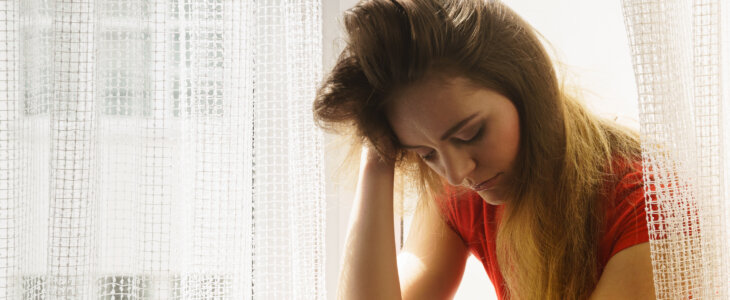 Anxiety and potential problems concept. Sad, unhappy worried brunette woman sitting on windowsill thinking about something depressing